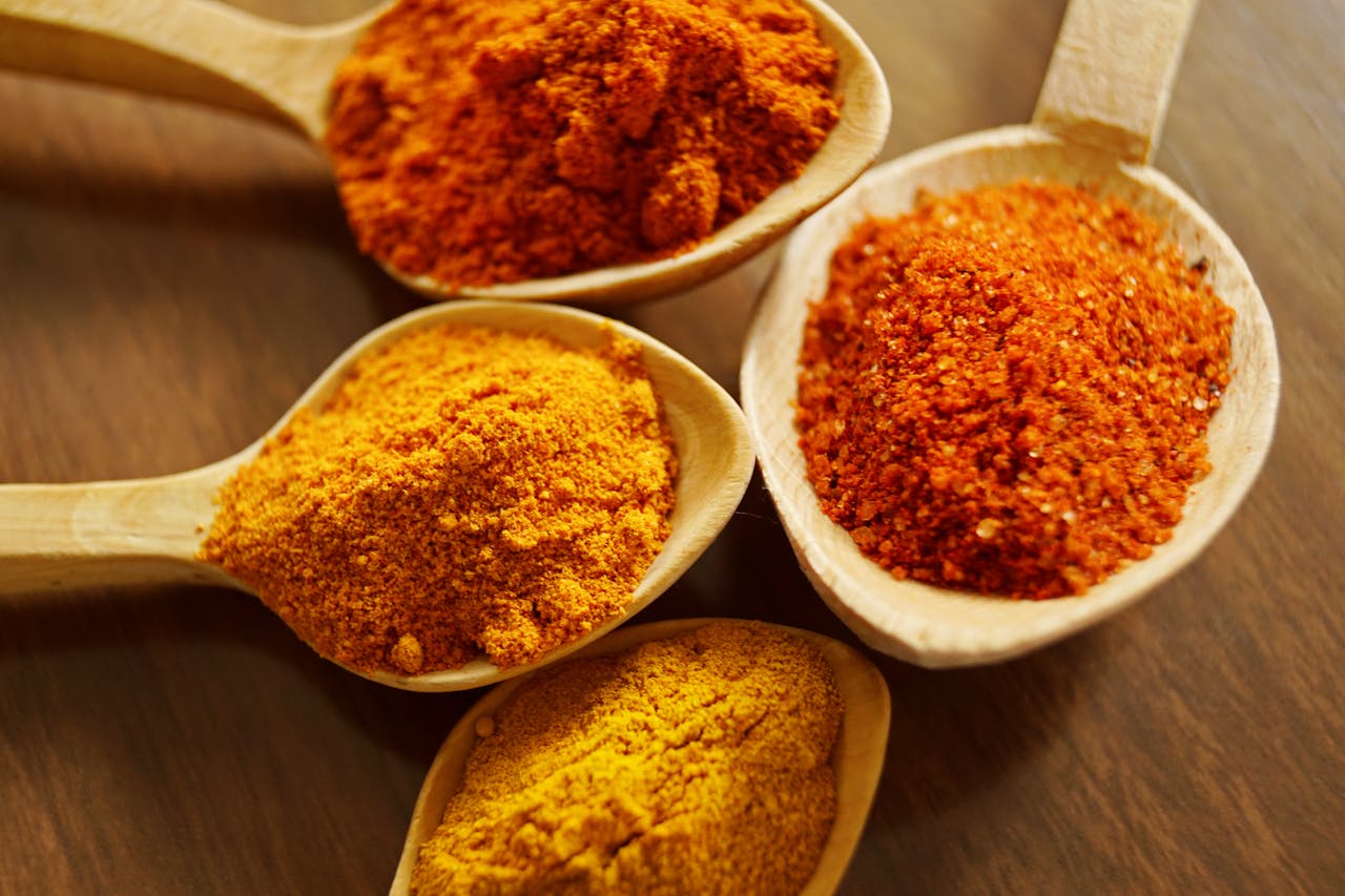 who-we-are Close-up of vibrant spices like turmeric and chili powder in wooden spoons.